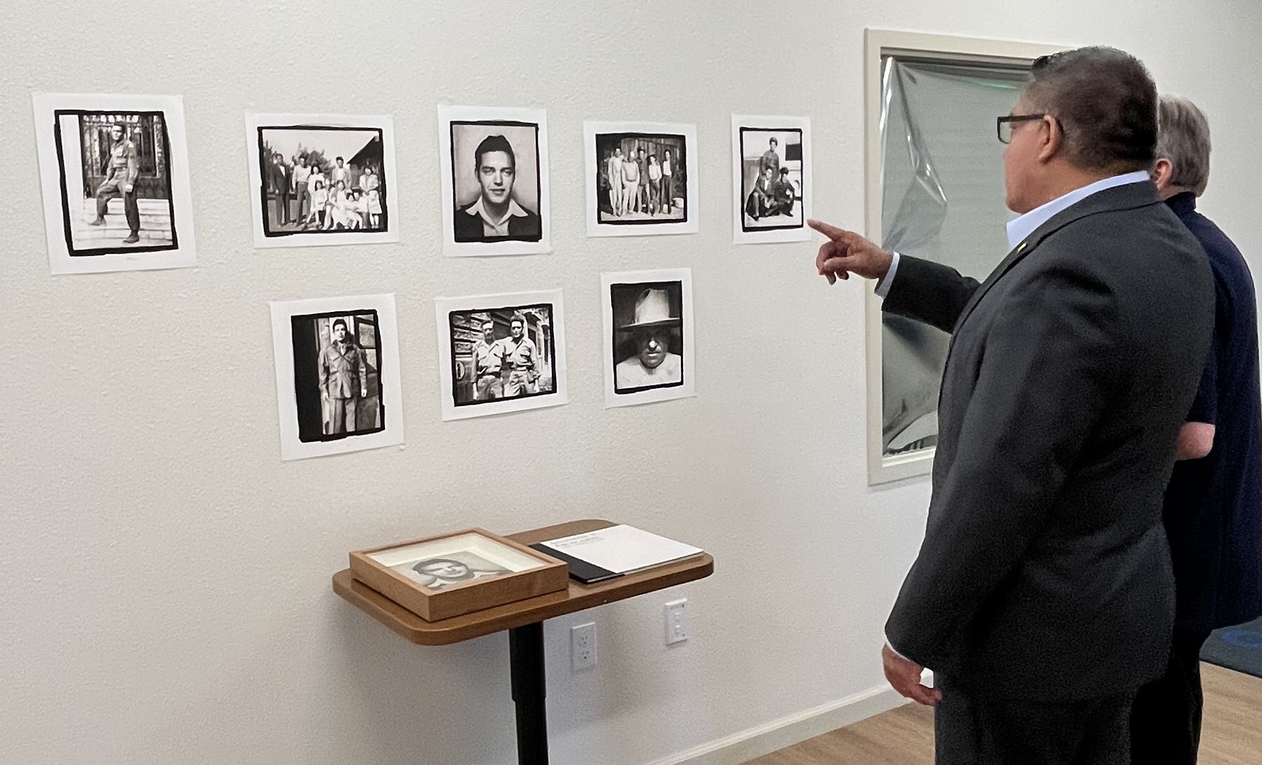 Two people looking at photos on a white wall.