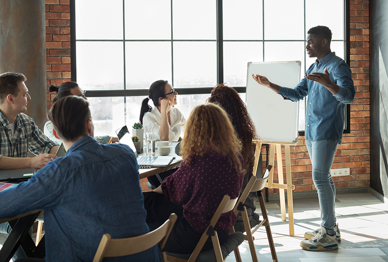 African-american team leader is lecturing his employees in loft office using white board